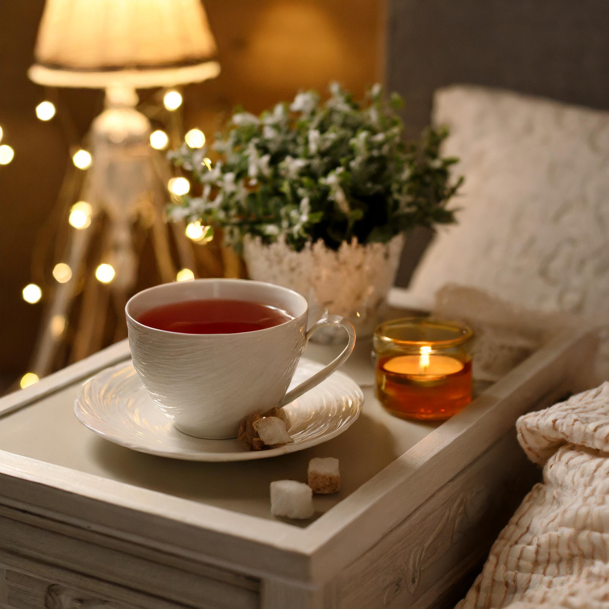 Thé Sommeil Nathéra Tasse de thé aux effets de sommeil, posée sur une table de nuit à coté d'un lit dans une ambiance chaleureuse et calme